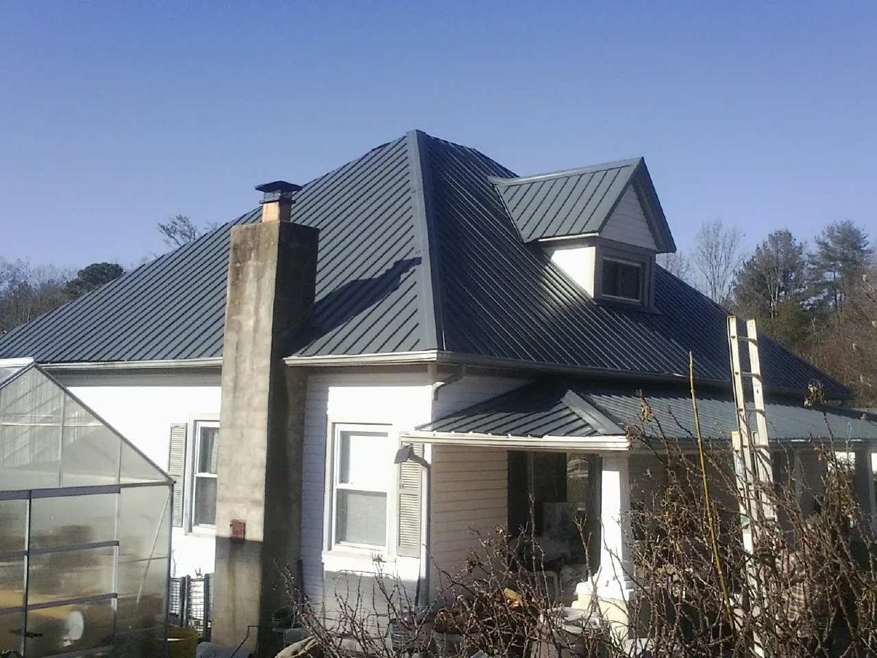Dark blue standing seam metal roof on a white farmhouse with dormer — Slate & Tile Roof Repair by Roofing Brothers in Fe Warren Afb