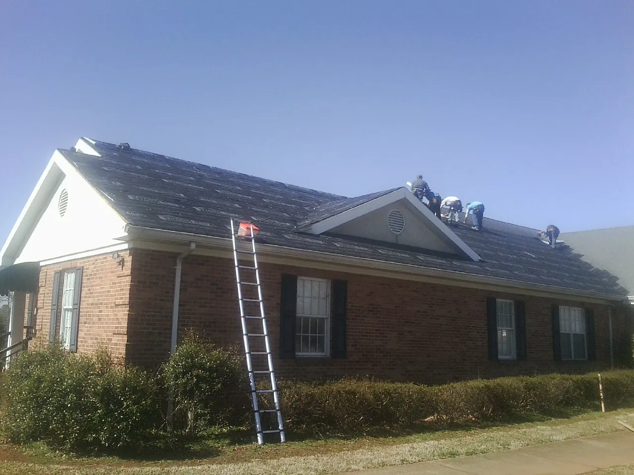Crew tearing shingles off a brick ranch roof with a ladder set — Emergency Roof Repair work by our crew in Fe Warren Afb