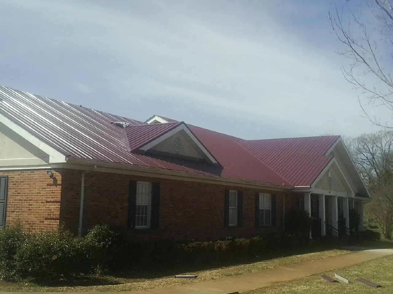 Red metal roof with gabled entries on a long brick building, from a Hail Damage Roof Repair job in Fe Warren Afb