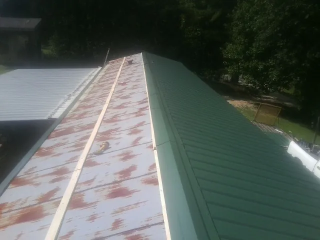 Old rusted panels beside newly installed green metal roofing — Wind Damage Roof Repair by Roofing Brothers in Fe Warren Afb