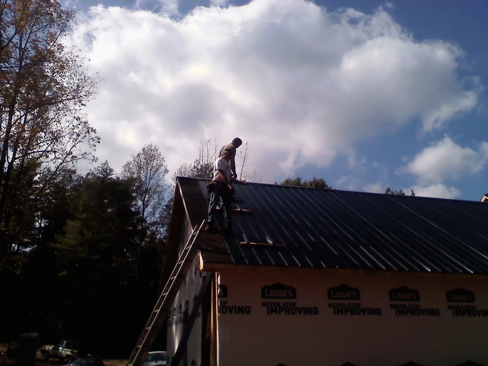 Roofer fastening dark metal panels high against a cloudy sky, from a Roof Inspection job in Fe Warren Afb