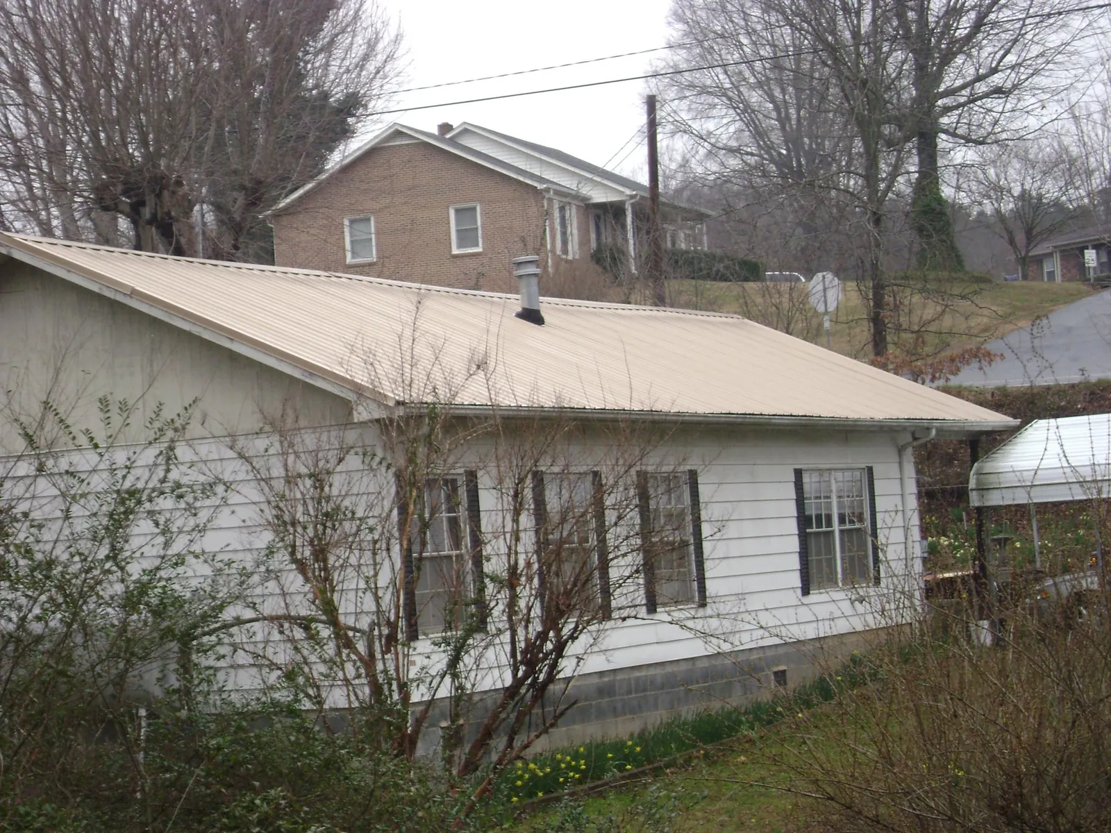 Tan metal roof on a white sided house set into a hillside — Commercial Roofing by Roofing Brothers in Fe Warren Afb